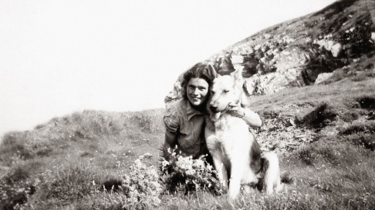 Foto antiga, em preto e branco, de uma moça com o cachorro numa encosta