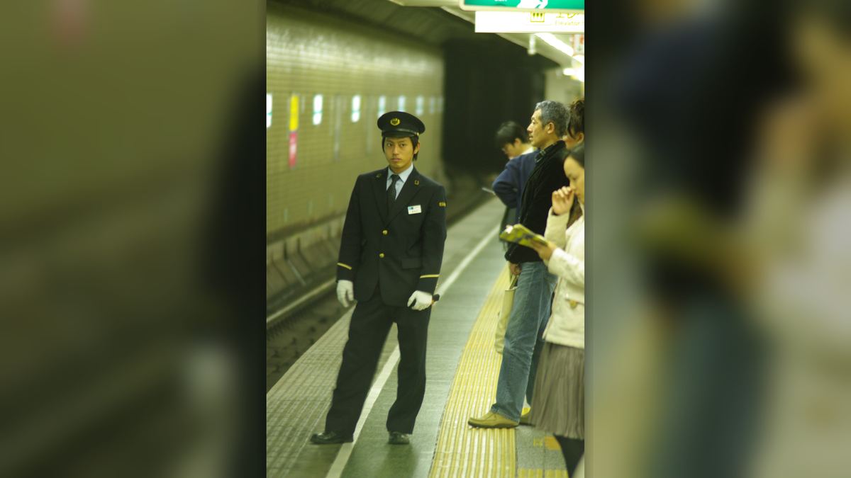 Um oshiya de quepe e luvas brancas na plataforma do metrô de Tóquio